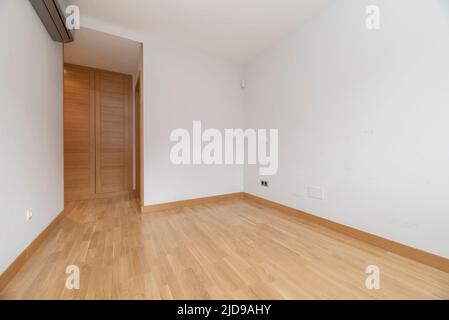 Leeres Zimmer mit eingebautem Eichenschrank, grauer Klimaanlage und hellem Eichenboden Stockfoto