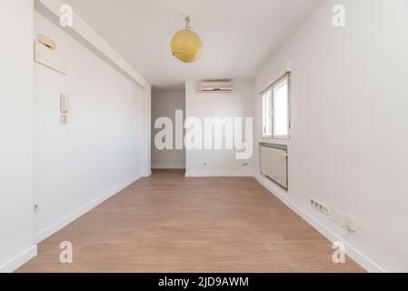 Leere Wohnung mit einem hellen Holzboden, einem Fenster zur Seite, einem Heizkörper in einer Nische unter dem Fenster und einer Klimaanlage, die an der Wand hängt Stockfoto