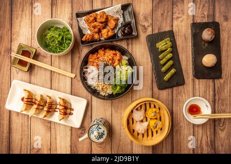 Set asiatischer Gerichte mit mochis, Lachs- und Seetang-Poke-Schüssel, Gyozas mit Sojasauce, Wakame-Algen, gedämpftem xiao Mai und Sojasauce in Schüsseln Stockfoto