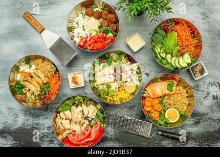 Set aus großen Metallschüsseln gefüllt mit gegrilltem Lachs, gegrilltem Hähnchen, rotem Thunfisch, Quinoa, mexikanischen Avocados, Geriebene Karotten, Kirschtomaten, Gurken, Stockfoto