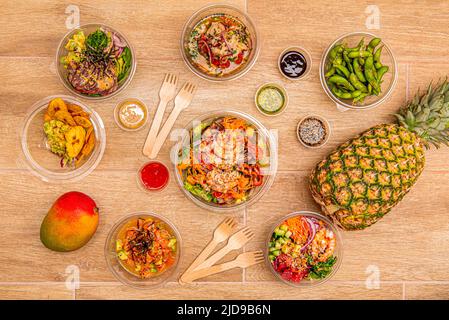 Draufsicht auf transparente Kunststoffschalen mit viel norwegischem Lachs, pilla, gebratenen Garnelen, Edamame, reifen Mango und Saucen Stockfoto