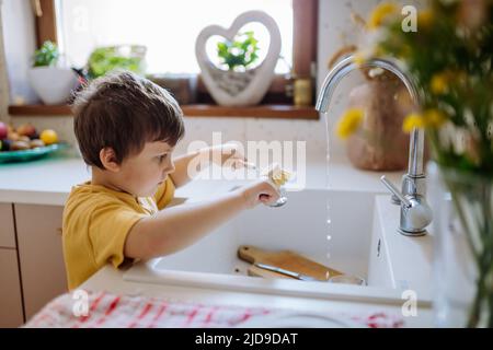 Kleiner Junge Waschbecher im Waschbecken in der Küche mit Holzpeeling, nachhaltige Lebenslaus. Stockfoto