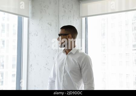 Afrikanischer Geschäftsmann, der im Wolkenkratzerbüro steht und auf die Stadt blickt Stockfoto
