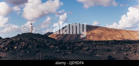 Frau, die sich mit den Händen in den Himmel erhebt und einen atemberaubenden Blick auf die vulkanische Landschaft im Timanfaya-Nationalpark auf Lanzarote, Spanien, genießt. Freiheit und Reisen Stockfoto