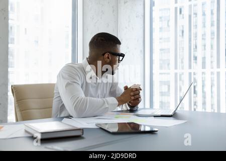 Afrikanischer Geschäftsmann sitzt am Arbeitsplatz und starrt aus dem Fenster Stockfoto