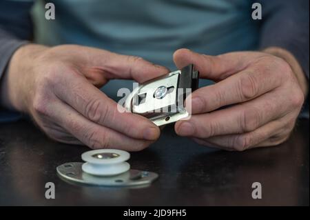 Ein gewachsener Mann hält eine Reihe von Möbelbeschlägen in den Händen. Obere Rollenhalterung für Schrankschiebesystem und untere Rolle für Schiebetüren. Möbel Stockfoto