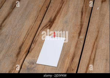 Eine leere Visitenkarte vor einem hölzernen Hintergrund. Ein weißes Papierrechteck wird mit einem Stecknadel an die alten Bretter gepingt. Selektiver Fokus. Stockfoto