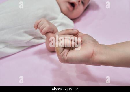 Nahaufnahme der schlafenden Babyhand in der Hand der Mutter auf dem Bett. Neues Familien- und Babyschlafkonzept Stockfoto
