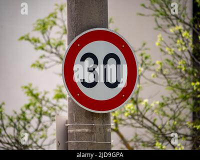 30 Geschwindigkeitsbegrenzungszeichen an einem durchgehenden Lichtpfosten. Deutsche Tempolimit in einer Stadt. Regeln für die Verkehrsteilnehmer. Die Verkehrsgeschwindigkeit darf nicht höher sein als 30 km/h. Stockfoto