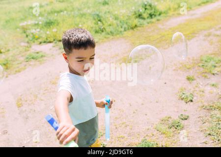 Vorschulkinder blasen an einem sonnigen Tag große Seifenblasen auf einem Feld Stockfoto