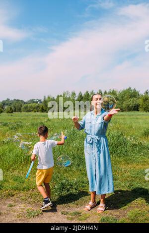 Mama und Sohn Vorschulkinder verbringen im Sommer Zeit im Freien und blasen große Seifenblasen Stockfoto