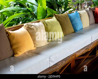 Reihe von vielen Farben der Kissen Dekoration auf dem Vintage-Holzsitz mit weißen Pads in der Nähe des grünen Gartens. Stockfoto