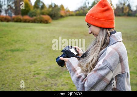 Mädchen mit Kamera sieht Foto. Junge Frau fotografiert im Frühling im Freien. Hobby, Freizeit Stockfoto