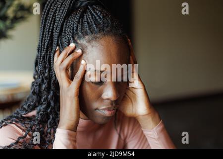 Junge afroamerikanische Frau, die mit geschlossenen Augen denkt und online am Laptop im Kaffeehaus arbeitet. Schwarzes Mädchen, das aus der Ferne arbeitet, freiberuflich, komfortabel Stockfoto