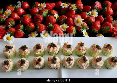 Gurkenbecher gefüllt mit Hummer-Salat mit Kaviar auf Tablett mit Erdbeeren verziert gekrönt. Stockfoto