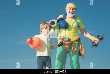 Sport für Kinder. Vater und Sohn sportlich - Familie Zeit zusammen. Älterer Mann und niedlicher kleiner Junge, der auf blauem Himmel Hintergrund trainiert - isoliert. Stockfoto