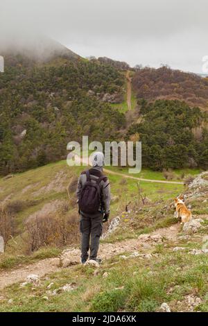 Ein Mann und ein Pembroke Welsh Corgi klettern über die Wolken hoch in den Bergen Stockfoto