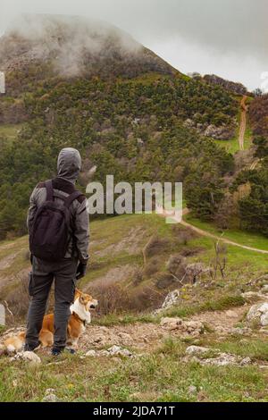 Ein Mann und ein Pembroke Welsh Corgi klettern über die Wolken hoch in den Bergen Stockfoto