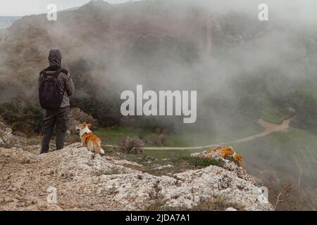 Ein Mann und ein Pembroke Welsh Corgi klettern über die Wolken hoch in den Bergen Stockfoto