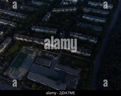 Luftaufnahme von Schulgebäuden in einem Wohnviertel in der Nähe von grünem Wald. Fliegen Sie in der Morgenstadt über die Straßen. Baumkronen-Ansicht auf Charkiw, Ukraine Stockfoto