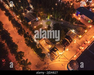 Luftaufnahme Nacht Vergnügungspark beleuchtete Attraktionen Aussicht. Kharkiv Stadt Erholungsgebiet in Abendlicht. Der Vergnügungspark Gorki Central Park schaut nach unten Stockfoto
