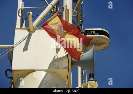 Die spanische Flagge flattert auf dem Navigationsmast mit Hupe und Leuchten des im Hafen von Valencia verankerten Handelscontainerschiffes. Stockfoto