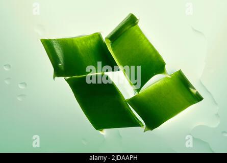 Draufsicht auf vier Stücke Aloe Vera, die auf einer waagerechten Fläche liegen. Sonnenlicht schimmert auf saftigen Scheiben Aloe-Blätter auf grünem Hintergrund. Hochwertige Fotos Stockfoto