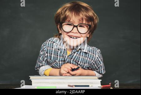 Zurück in die Schule und glückliche Zeit. Lustiger kleiner Junge in Brille auf Tafel Hintergrund. Kind mit einem Buch. Stockfoto