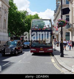London, Greater London, England, Juni 08 2022: Touristen sitzen in einem Open-Top-Bus auf einer Straße mit einem Taxi daneben. Stockfoto