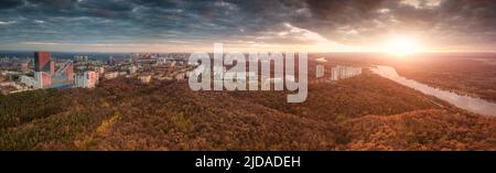 Luftaufnahme eines farbenfrohen herbstlichen Stadtparks und Wohnblocks mit Gebäuden. Lebhafter und heller Sonnenuntergang über dem Fluss Stockfoto