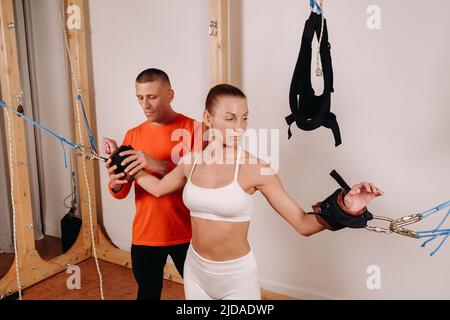 Der Trainer fixiert die Hände, um mit dem Training auf dem Simulator für die Dehnung des menschlichen Körpers zu beginnen. Stockfoto