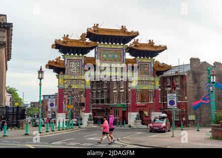 Zwei Personen, die am chinesischen Torbogen, Tor oder Paifang am Eingang zu Liverpools Chinatown in der Nelson Street vorbeigehen. England, Großbritannien Stockfoto
