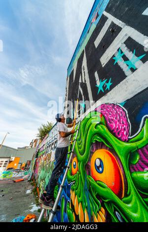 Mr KEOS, ein Straßenkünstler, der Farbe auf die Wand des Skateparks in der Jamaica Street, Baltic Triangle, Liverpool, Großbritannien, aufgetragen hat Stockfoto