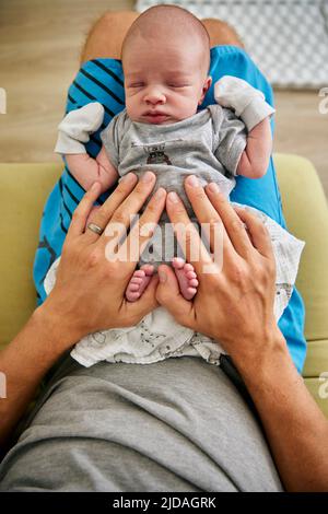 Aufnahme der Hände des Vaters, die auf dem schlafenden drei Monate alten Jungen mit Fäustlingen ruhen Stockfoto