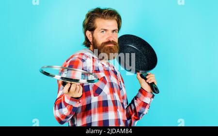 Bärtiger Mann mit Frypan. Männlicher Koch mit Bratpfanne und Deckel. Küchenutensilien. Kochutensilien. Stockfoto