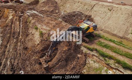 Eine gelbe und schwarze Industriemaschine, die während der Arbeiten auf einer Baustelle ein Loch in einen braunen Sand gräbt. Hochwertige Fotos Stockfoto