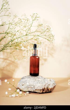 Bernsteinfarbene Glas-Serumflasche auf Naturstein mit Gipsophila-Blüten. Neutraler beigefarbener Hintergrund. Beauty, Hautpflege Konzept. Vorderansicht. Stockfoto