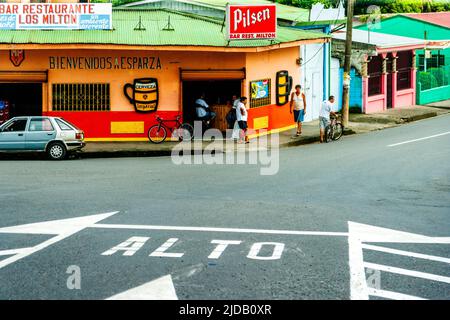 Costa Rica Kreuzung mit einer Bar auf der anderen Straßenseite, wo eine Gruppe von Männern Bier trinken. Stockfoto