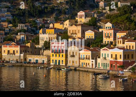 Warmes Sonnenlicht auf den farbenfrohen Gebäuden entlang der Uferpromenade in Gialos Harbor, Symi (Simi) Insel; Dodekanese Island Group, Griechenland Stockfoto