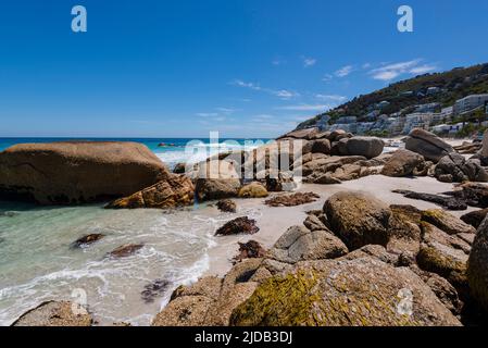 Große Felsbrocken entlang der felsigen Küste mit Strandgebäuden am Hügel von Clifton Beach; Kapstadt, Westkap, Südafrika Stockfoto