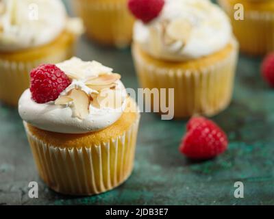 Viele appetitliche Muffins mit Rahm, Himbeeren und Mandeln auf grünem Hintergrund. Große Gruppe von Objekten. Food Design, Restaurant, Hotel, Cafe, patis Stockfoto