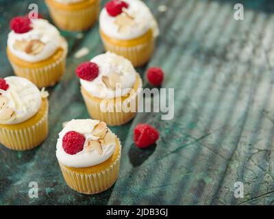 Leichte, frische Muffins mit Creme, verziert mit Himbeeren und Mandeln auf einer grünen Serviette. Hintergrund der Speisen. Food Design, Süßes Essen, Urlaub, Geburtstag, Stockfoto