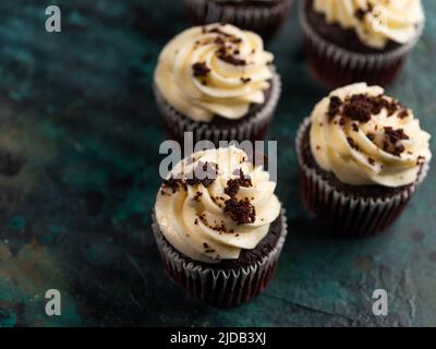 Chocolate Cupcakes - Brownies mit Creme, verziert mit Schokoladenstückchen auf einem dunkelgrünen Hintergrund. Festliche Leckerbissen zum Geburtstag, Jubiläum, Hochzeit. Stockfoto