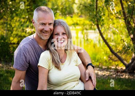 Außenporträt eines erwachsenen Ehepaars, das in einem Park in Edmonton, Alberta, Kanada, auf dem Rasen sitzt Stockfoto