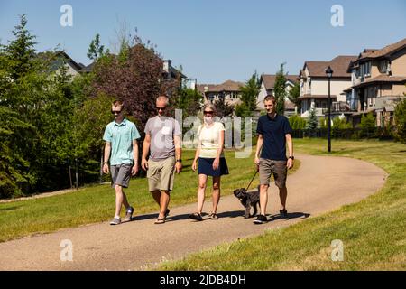 Eine Familie mit zwei Söhnen im Teenageralter spaziert an einem schönen sonnigen Tag mit ihrem Hund in einem Park in Edmonton, Alberta, Kanada Stockfoto