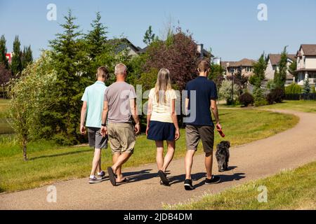 Eine Familie mit zwei Söhnen im Teenageralter spaziert an einem schönen sonnigen Tag mit ihrem Hund in einem Park in Edmonton, Alberta, Kanada Stockfoto