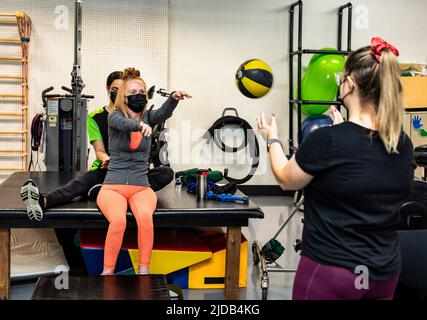 Eine querschnittsgelähmte Frau, die beim Training mit ihren Trainern Medizinball macht: Edmonton, Alberta, Kanada Stockfoto