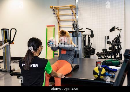 Eine Querschnittsgelähmte Frau, die während ihres Workouts mit ihrem Trainer in Edmonton, Alberta, Kanada, bilaterale Aufstiege macht Stockfoto