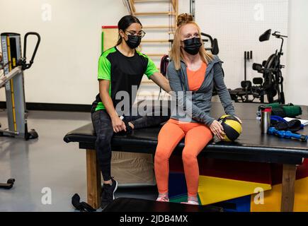 Eine querschnittsgelähmte Frau, die beim Training mit ihren Trainern Medizinball macht: Edmonton, Alberta, Kanada Stockfoto