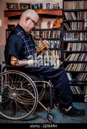 Ein Mann mit zwei Gliedmaßenamputationen, der zu Hause Trompete spielt Albert, Alberta, Kanada Stockfoto